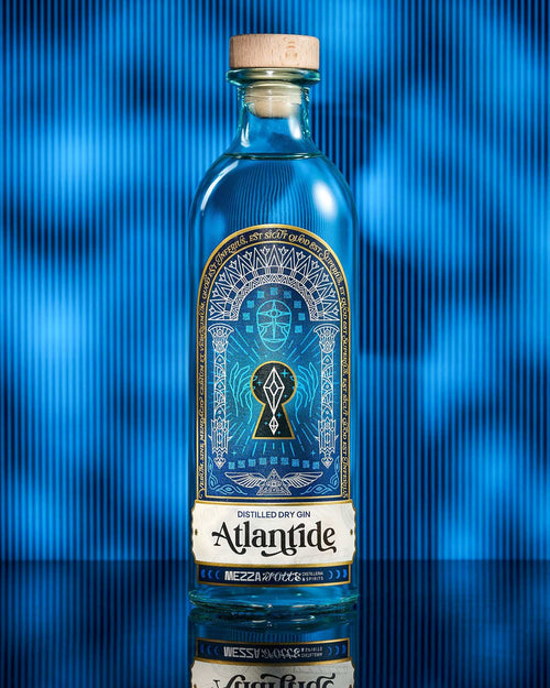 Bottiglia di Atlantide Distilled Dry Gin Mezzanotte con etichetta artistica blu e oro raffigurante un portale mistico, su sfondo blu. Gin artigianale italiano.