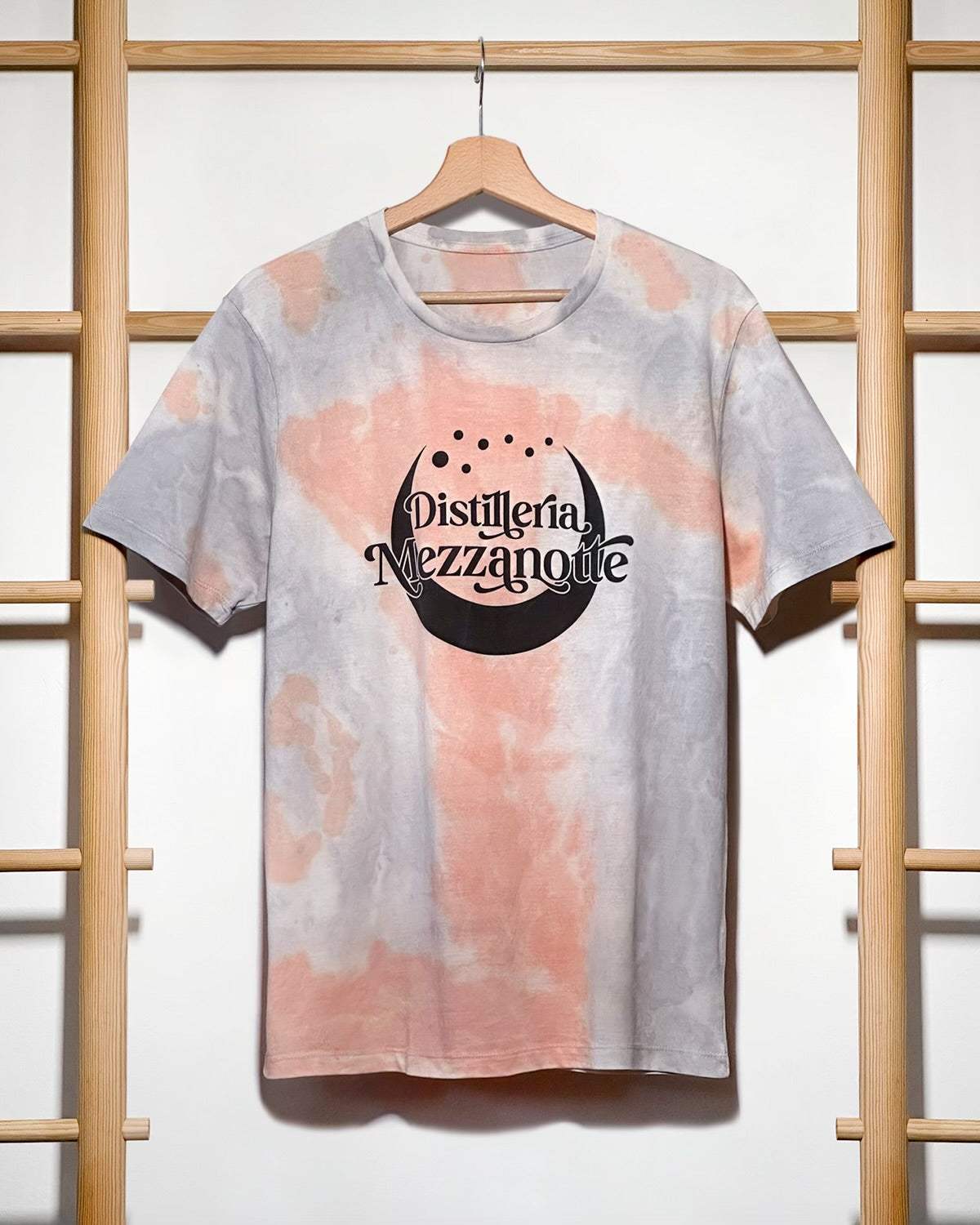 T-shirt tie-dye Distilleria Mezzanotte rosa grigio con logo luna minimalista su gruccia legno